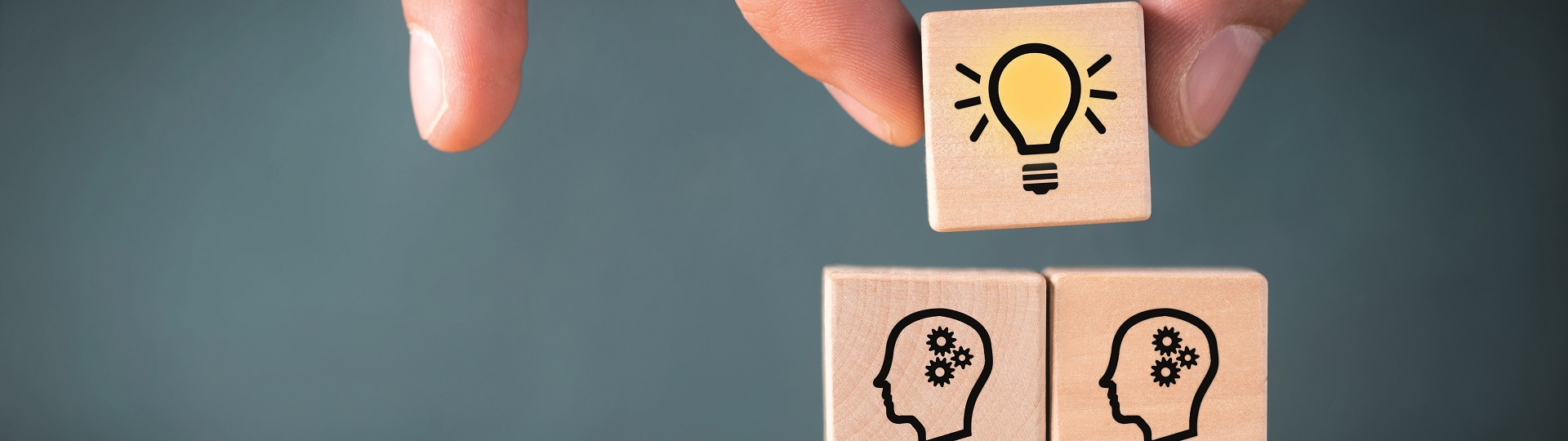 Holzklötze mit Glühbirne und Köpfen mit Zahnrädern als Symbol für Ideen und Intelligenz.