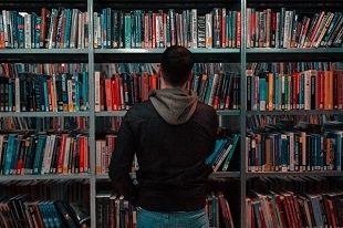 Person wearing black and gray jacket in front of bookshelf photo